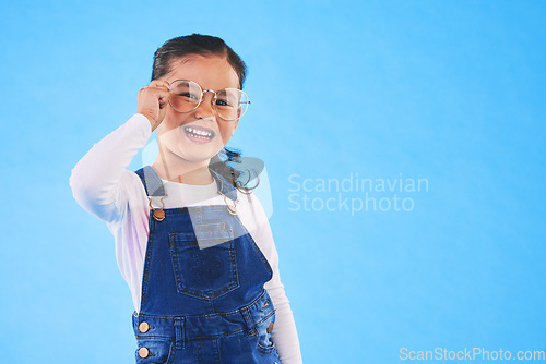 Image of Girl child, glasses and frame in studio portrait for vision, health and eye care by blue background. Female kid, test spectacles and young fashion model with lens, smile or eyesight with mockup space