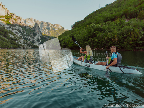 Image of A young couple enjoying an idyllic kayak ride in the middle of a beautiful river surrounded by forest greenery