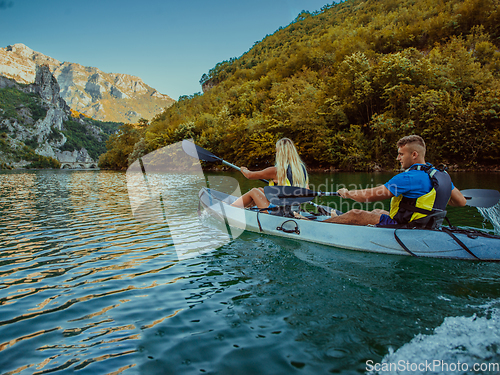 Image of A young couple enjoying an idyllic kayak ride in the middle of a beautiful river surrounded by forest greenery