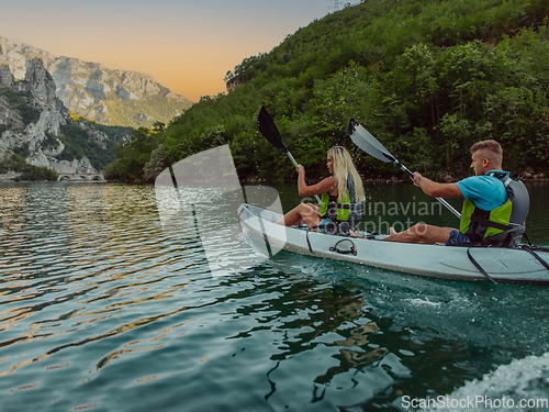 Image of A young couple enjoying an idyllic kayak ride in the middle of a beautiful river surrounded by forest greenery