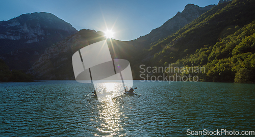 Image of A group of friends enjoying fun and kayaking exploring the calm river, surrounding forest and large natural river canyons during an idyllic sunset.