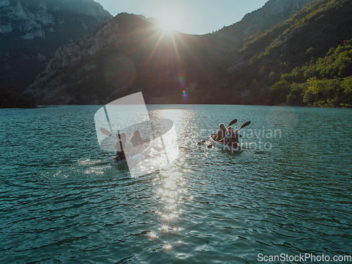 Image of A group of friends enjoying fun and kayaking exploring the calm river, surrounding forest and large natural river canyons during an idyllic sunset.