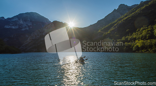 Image of A group of friends enjoying fun and kayaking exploring the calm river, surrounding forest and large natural river canyons during an idyllic sunset.