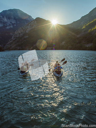 Image of A group of friends enjoying fun and kayaking exploring the calm river, surrounding forest and large natural river canyons during an idyllic sunset.