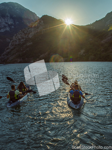 Image of A group of friends enjoying fun and kayaking exploring the calm river, surrounding forest and large natural river canyons during an idyllic sunset.