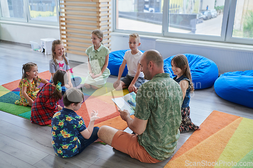 Image of Reading time in an elementary school or kindergarten, a teacher reading a book to children in an elementary school or kindergarten. The concept of pre-school education. Selective focus