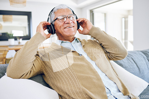 Image of Senior man, headphones and listening to music in home, living room and relax on lounge sofa with podcast, radio or sound. Streaming, jazz song and audio with earphones and mobile technology in house