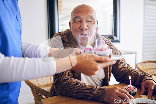 Image of Celebration, blowing candles and a man with a caregiver, cupcake and birthday in a nursing home. Happy, house and a senior person or patient with cake or food from a healthcare employee for a party