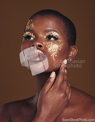 Image of Art, aesthetic and black woman with gold makeup and brown background with glitter, paint and cosmetics. Shine, glow and African model in studio for beauty, fashion and freedom in luxury skincare.