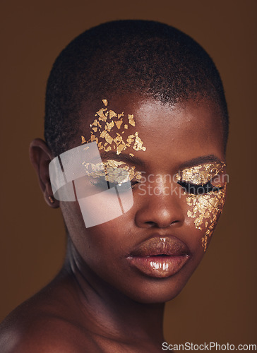 Image of Gold flakes, beauty and black woman with face closeup with makeup and cosmetics in studio. Brown background, African female model and glitter with golden shine and glow from facial paint sparkle