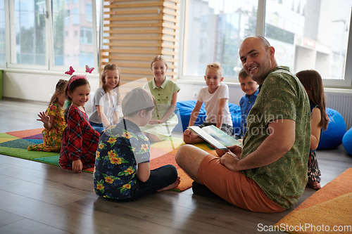 Image of Reading time in an elementary school or kindergarten, a teacher reading a book to children in an elementary school or kindergarten. The concept of pre-school education. Selective focus