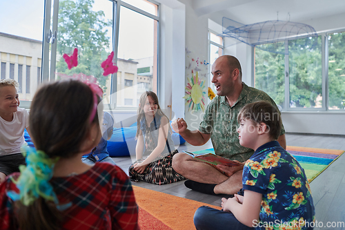 Image of Reading time in an elementary school or kindergarten, a teacher reading a book to children in an elementary school or kindergarten. The concept of pre-school education. Selective focus