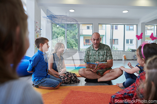 Image of Reading time in an elementary school or kindergarten, a teacher reading a book to children in an elementary school or kindergarten. The concept of pre-school education. Selective focus