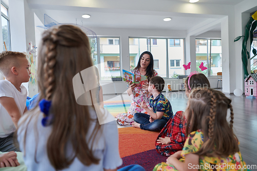 Image of Reading time in an elementary school or kindergarten, a teacher reading a book to children in an elementary school or kindergarten. The concept of pre-school education. Selective focus