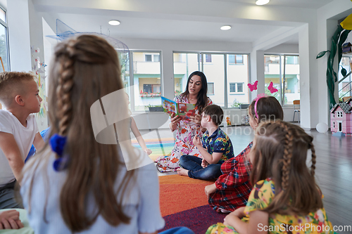 Image of Reading time in an elementary school or kindergarten, a teacher reading a book to children in an elementary school or kindergarten. The concept of pre-school education. Selective focus