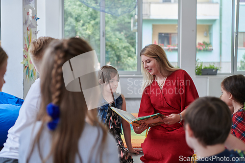 Image of Reading time in an elementary school or kindergarten, a teacher reading a book to children in an elementary school or kindergarten. The concept of pre-school education. Selective focus