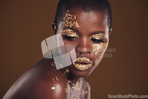 Image of Art, studio and black woman with gold makeup on brown background, glitter paint facial and cosmetics. Shine, glow and face of African model for beauty, fashion or aesthetic freedom in luxury skincare