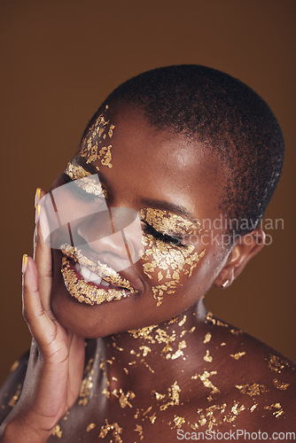 Image of Black woman, face and gold makeup with luxury glow and skincare mask with glitter. Sparkle, smile and beauty with rich and shine of cosmetics and model in studio with facial art with brown background