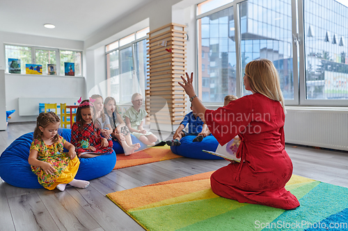 Image of A happy female teacher sitting and playing hand games with a group of little schoolchildren