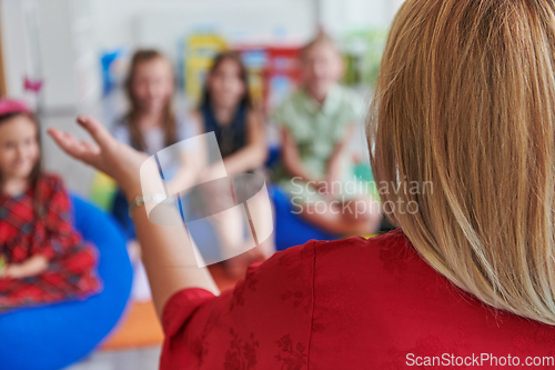 Image of A happy female teacher sitting and playing hand games with a group of little schoolchildren