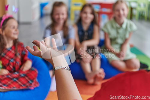 Image of A happy female teacher sitting and playing hand games with a group of little schoolchildren