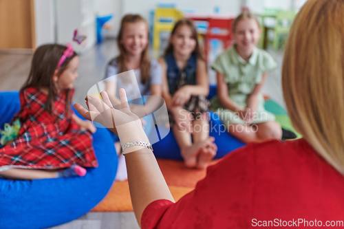 Image of A happy female teacher sitting and playing hand games with a group of little schoolchildren