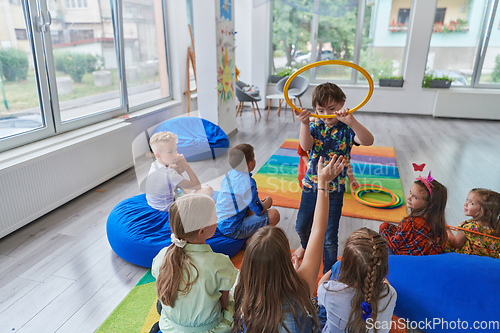 Image of A happy female teacher sitting and playing hand games with a group of little schoolchildren