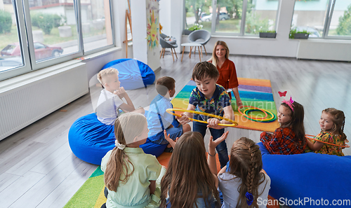 Image of A happy female teacher sitting and playing hand games with a group of little schoolchildren