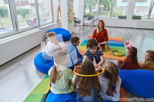 Image of A happy female teacher sitting and playing hand games with a group of little schoolchildren