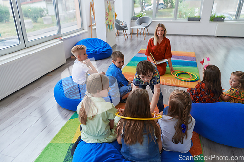 Image of A happy female teacher sitting and playing hand games with a group of little schoolchildren