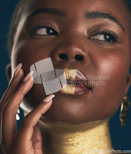 Image of Face, beauty and black woman in gold for culture, heritage or tradition on a blue background in studio. Skincare, makeup and african style with a young model closeup for elegance or cosmetics