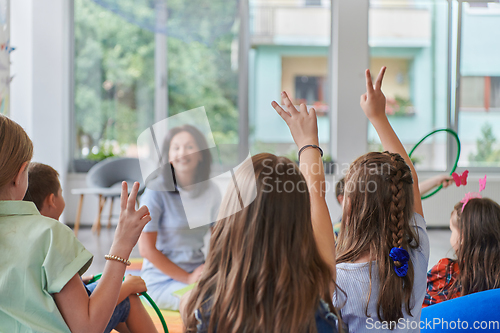 Image of A happy female teacher sitting and playing hand games with a group of little schoolchildren