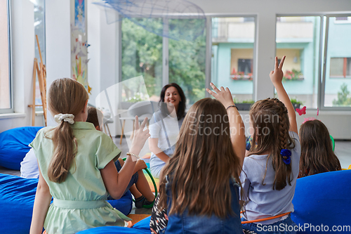 Image of A happy female teacher sitting and playing hand games with a group of little schoolchildren