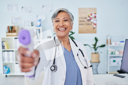 Image of Happy mature woman, doctor and infrared thermometer in checking temperature or fever at hospital. Senior female person, medical or healthcare professional smile with laser scanner for flu screening