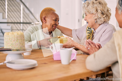 Image of Senior friends, birthday cake and women celebration at a home with a present and gift with people. Surprise, giving and party of elderly group at a dining room table together in retirement with smile