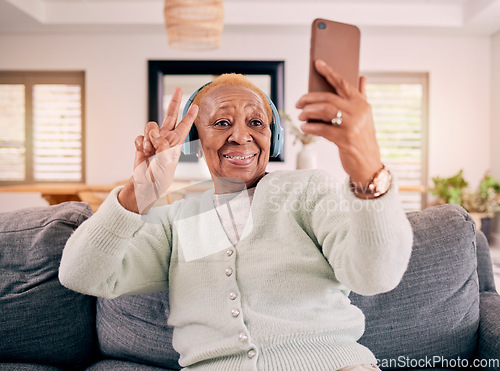 Image of Headphones, selfie and senior woman with peace sign in home listening to music, audio and radio on sofa. Retirement, emoji and happy person in living room take photo for social media and online post