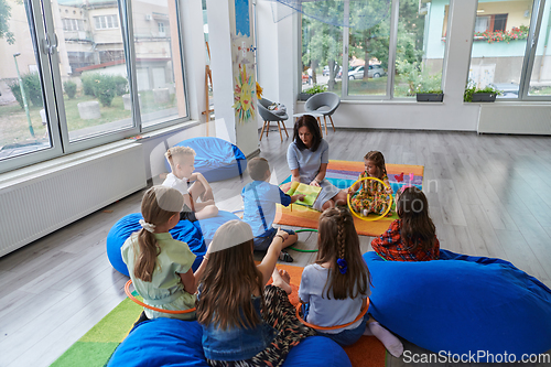 Image of A happy female teacher sitting and playing hand games with a group of little schoolchildren