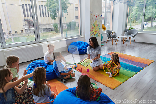 Image of A happy female teacher sitting and playing hand games with a group of little schoolchildren