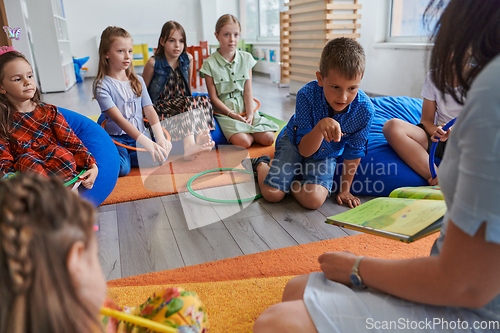 Image of A happy female teacher sitting and playing hand games with a group of little schoolchildren