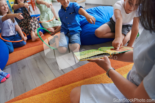 Image of A happy female teacher sitting and playing hand games with a group of little schoolchildren