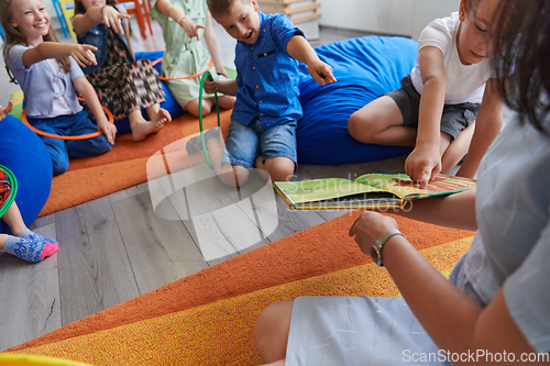 Image of A happy female teacher sitting and playing hand games with a group of little schoolchildren