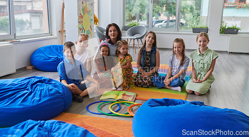 Image of A happy female teacher sitting and playing hand games with a group of little schoolchildren