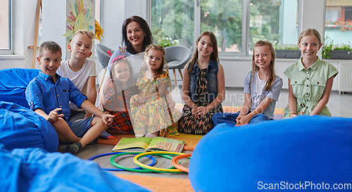 Image of A happy female teacher sitting and playing hand games with a group of little schoolchildren