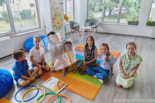 Image of A happy female teacher sitting and playing hand games with a group of little schoolchildren