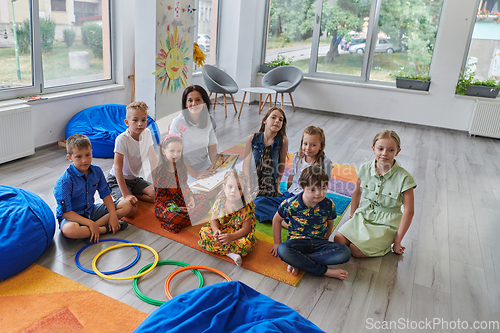 Image of A happy female teacher sitting and playing hand games with a group of little schoolchildren