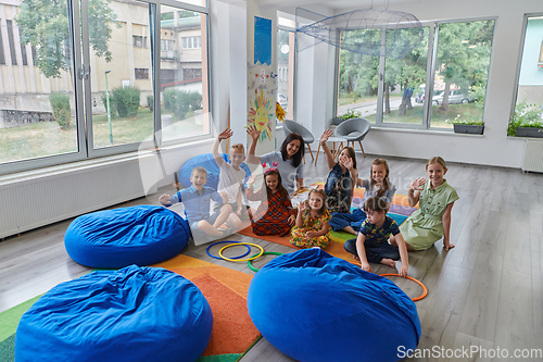 Image of A happy female teacher sitting and playing hand games with a group of little schoolchildren