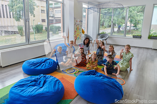 Image of A happy female teacher sitting and playing hand games with a group of little schoolchildren