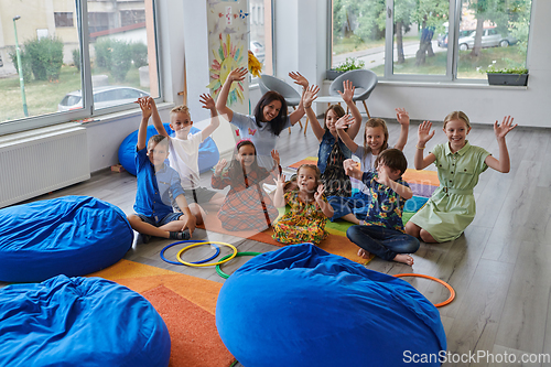 Image of A happy female teacher sitting and playing hand games with a group of little schoolchildren