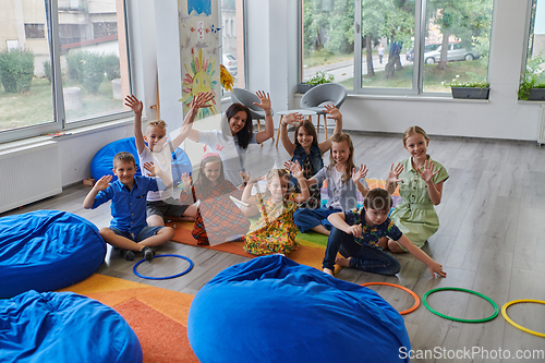 Image of A happy female teacher sitting and playing hand games with a group of little schoolchildren