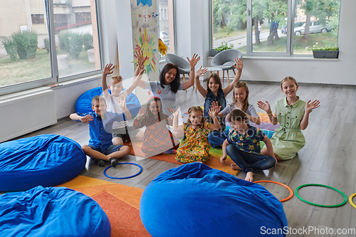 Image of A happy female teacher sitting and playing hand games with a group of little schoolchildren